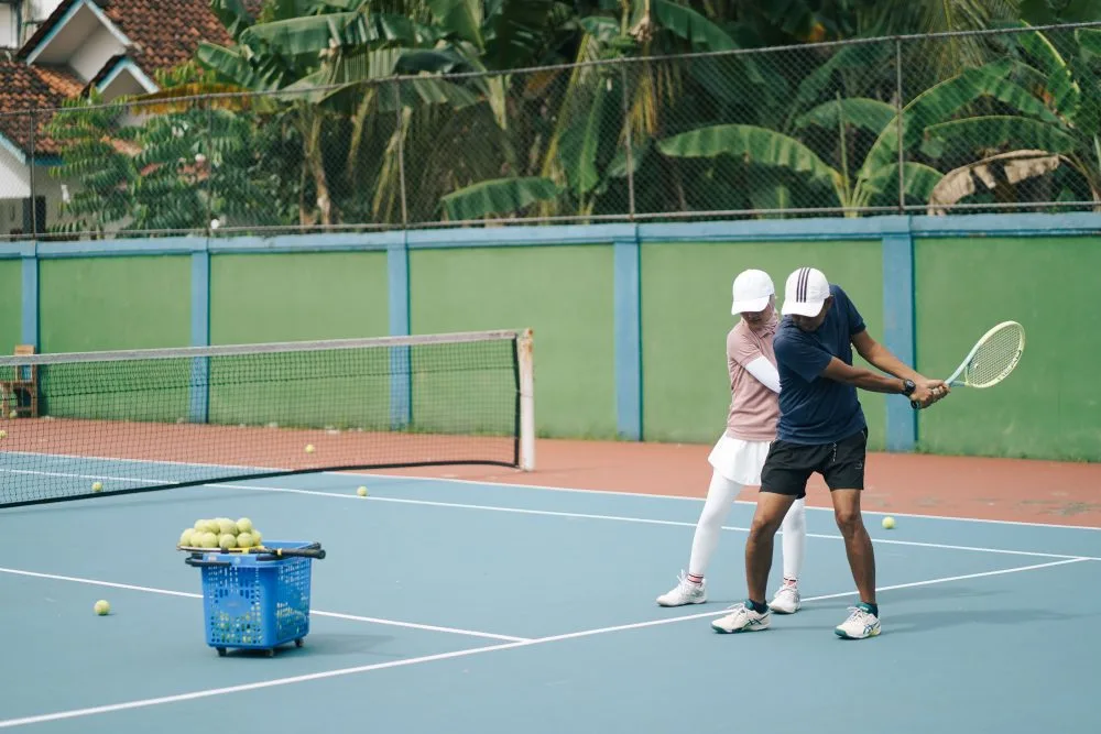 Tennistrainer geeft les op een buitenbaan